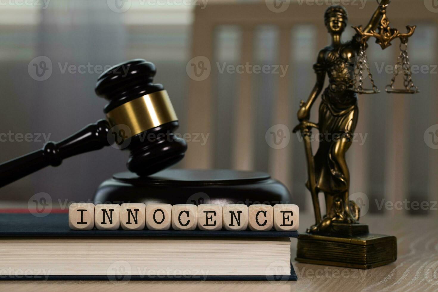 Word INNOCENCE composed of wooden dices. Wooden gavel and statue of Themis in the background. photo