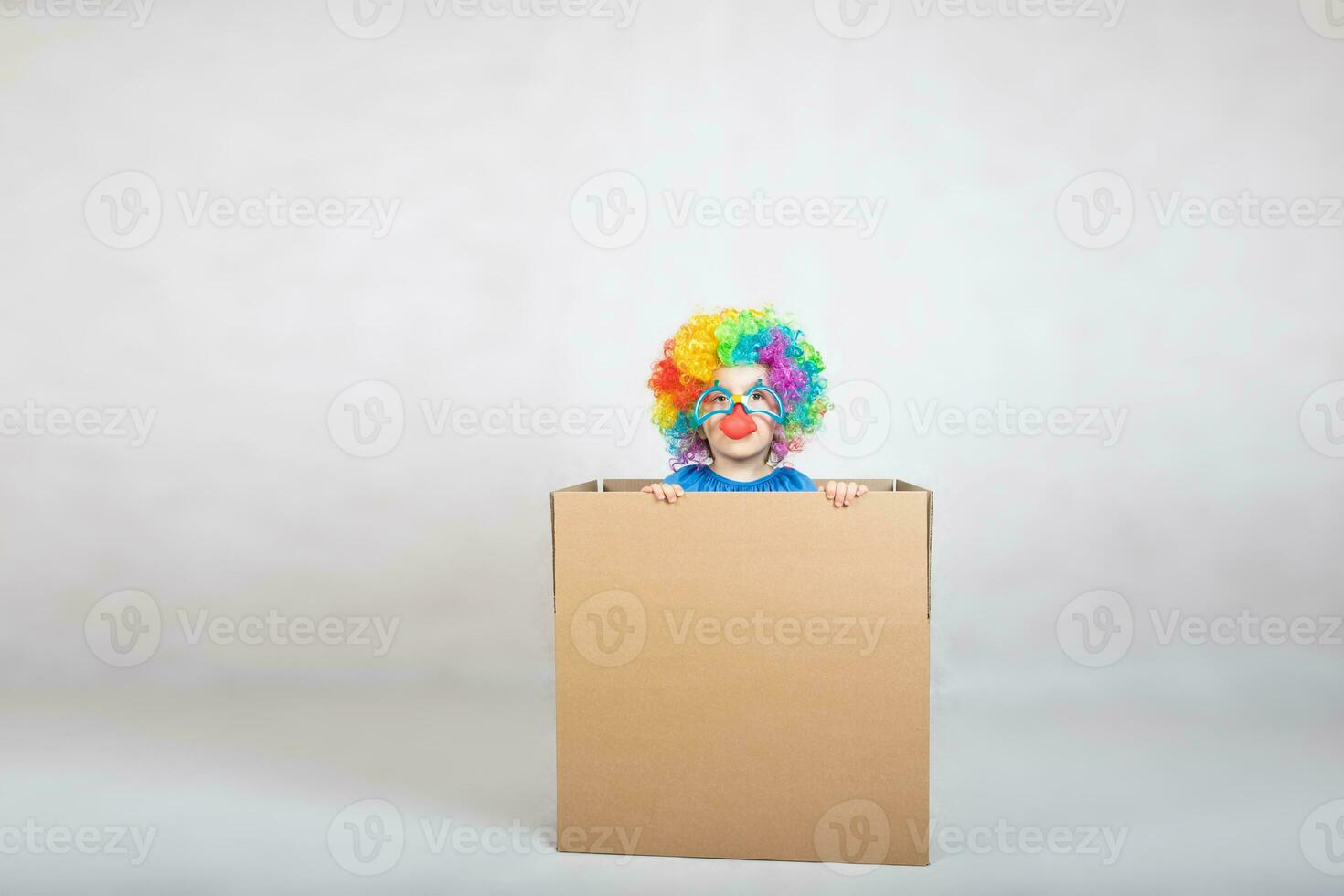 Boy of five years dressed in the costume of a clown stays in a carton paper box. photo