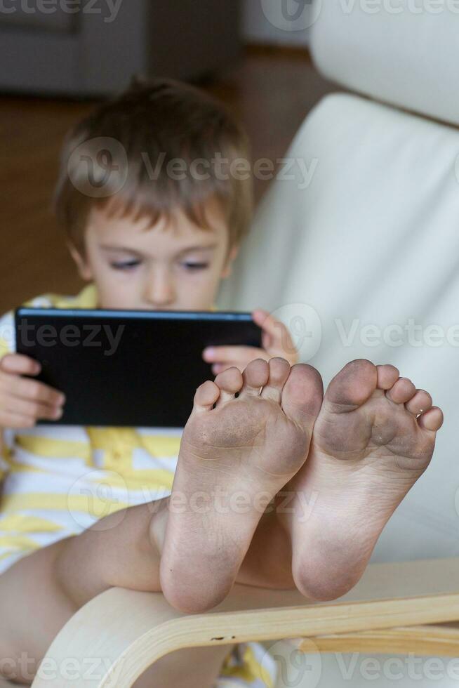 Dirty feet of sitting in the arm chair with his tablet. photo