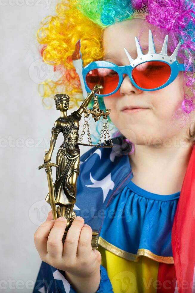 Statue of Themis in the hand of five years old child dressed in clown costume. photo