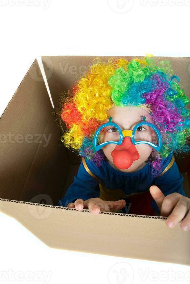 Boy of five years dressed in the costume of a clown stays in a carton paper box. photo