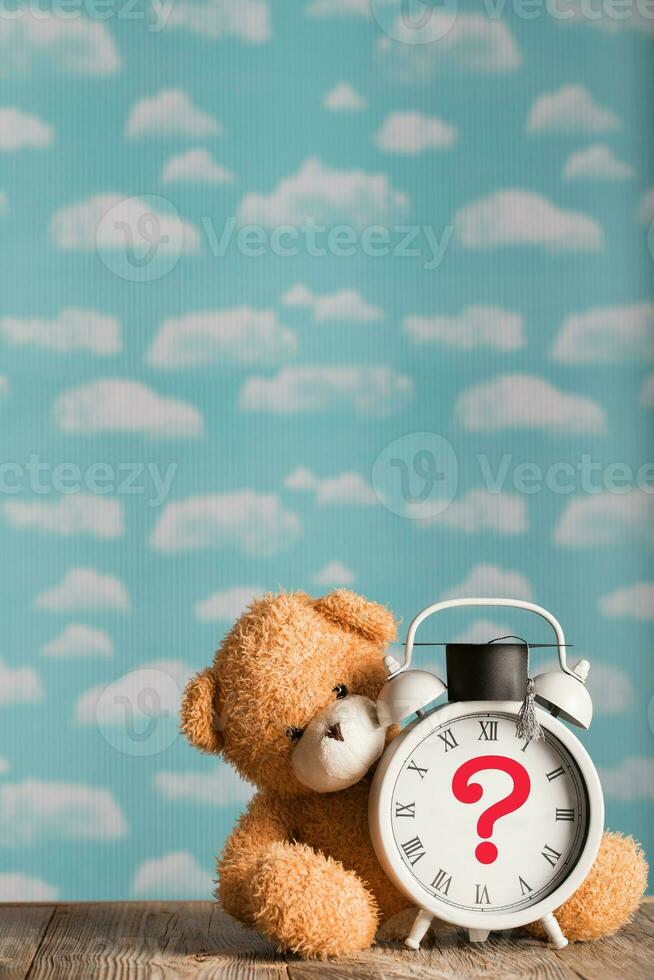 Question mark depicted on a vintage clock with academic cap. Brown plush teddy bear in the background. photo