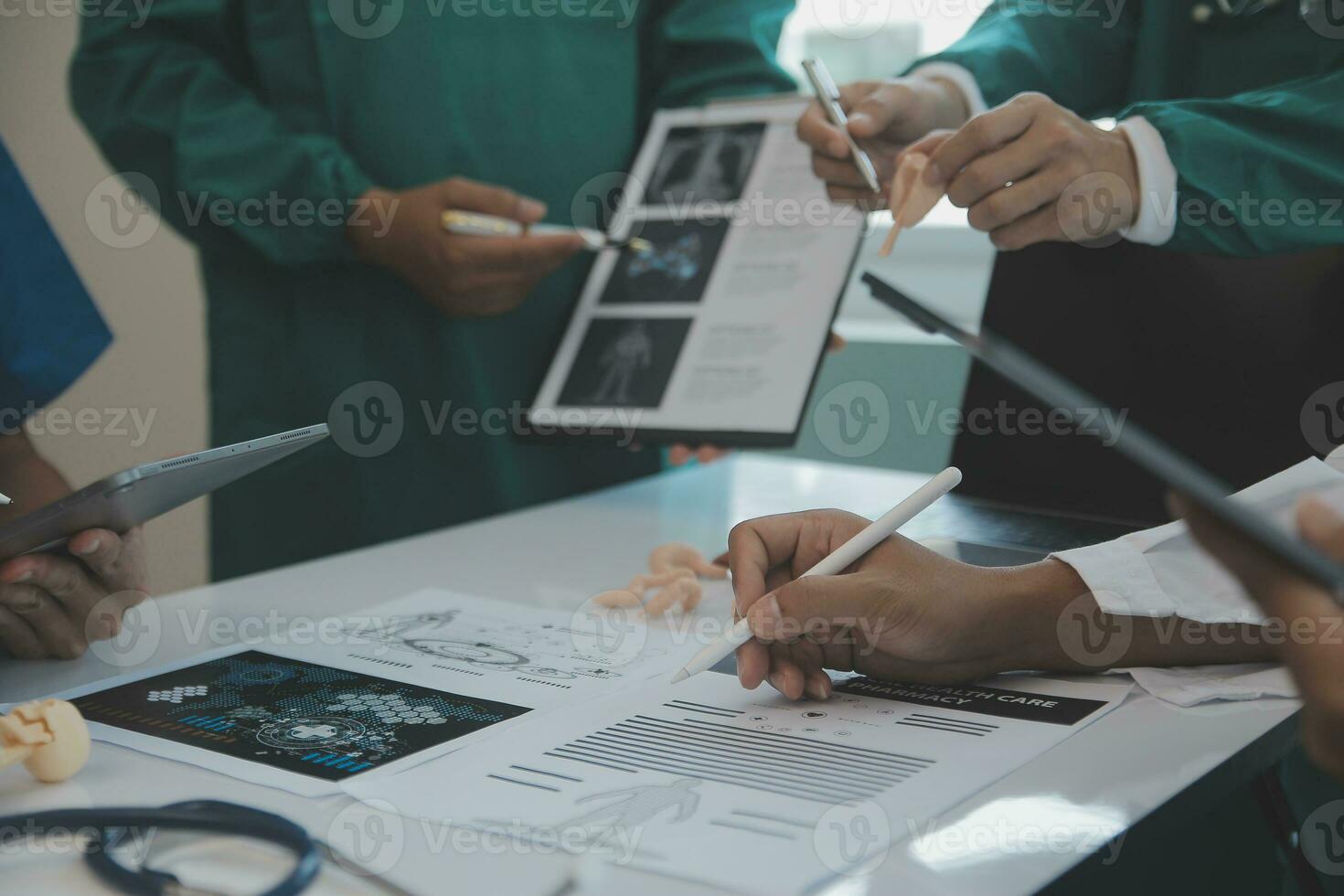 Multiracial team of doctors discussing a patient standing grouped in the foyer looking at a tablet computer, close up view photo