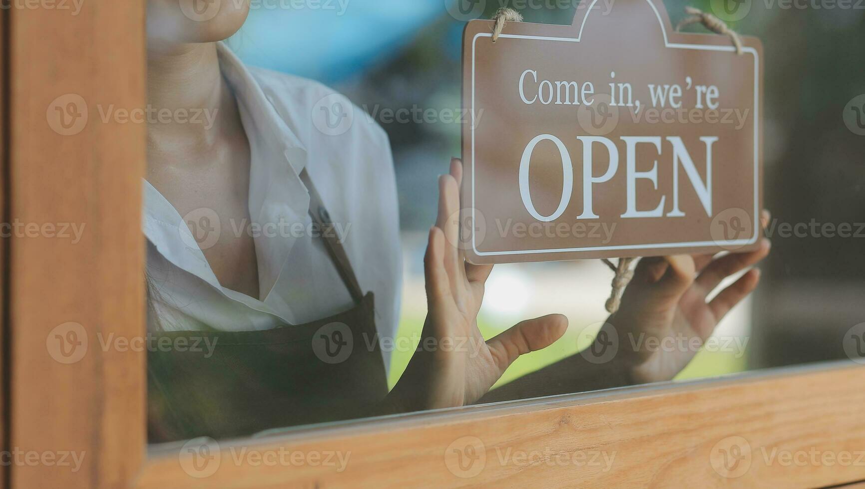 Young entrepreneur holding open sign on glass door at cafe photo