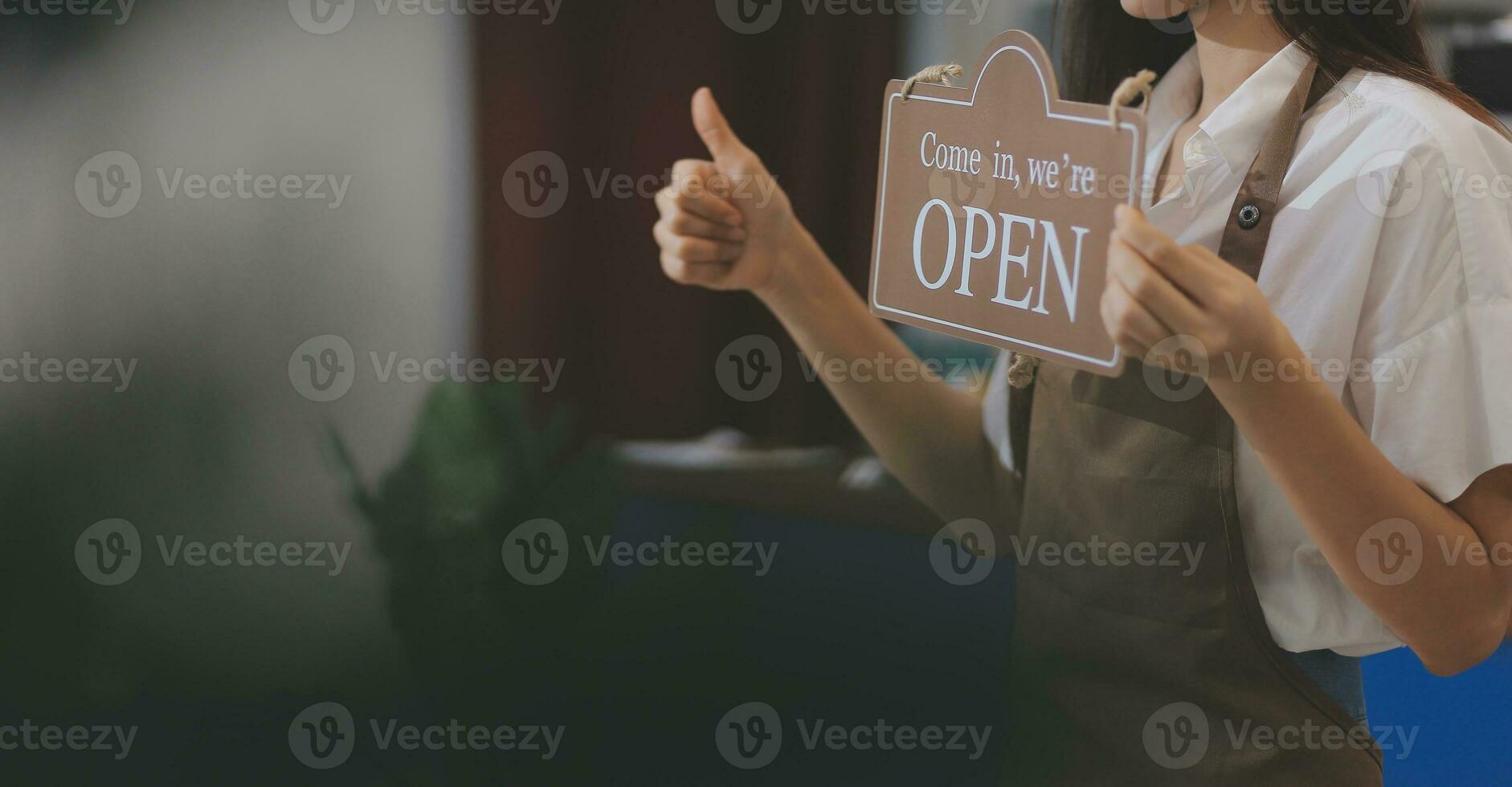 Young entrepreneur holding open sign on glass door at cafe photo