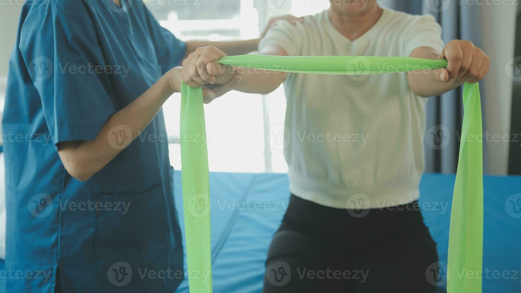 Happy senior woman doing exercise at home with physiotherapist. Old retired lady doing stretching arms at home with the help of a personal trainer during a rehabilitation session. photo