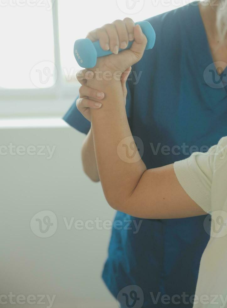 Happy senior woman doing exercise at home with physiotherapist. Old retired lady doing stretching arms at home with the help of a personal trainer during a rehabilitation session. photo