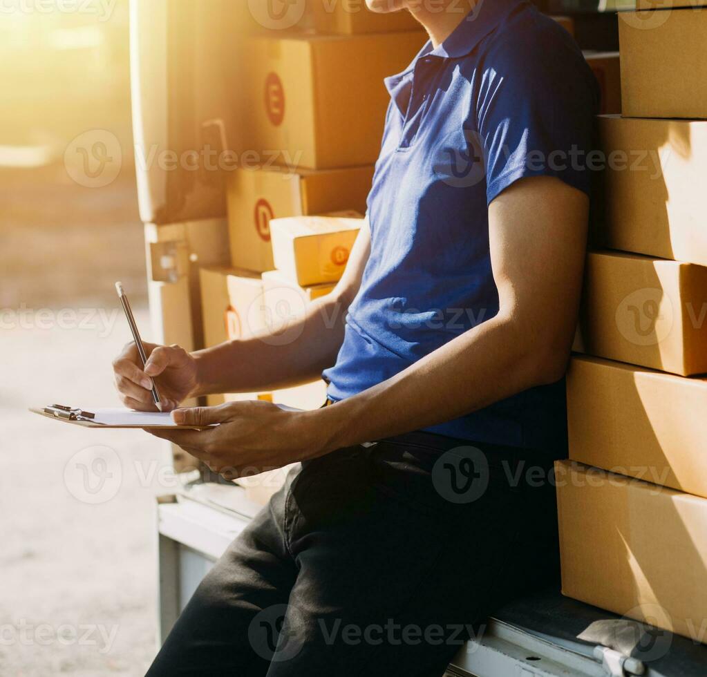 Delivery man with cardboard box checking document list In van and parcels on seat outside the warehouse. photo