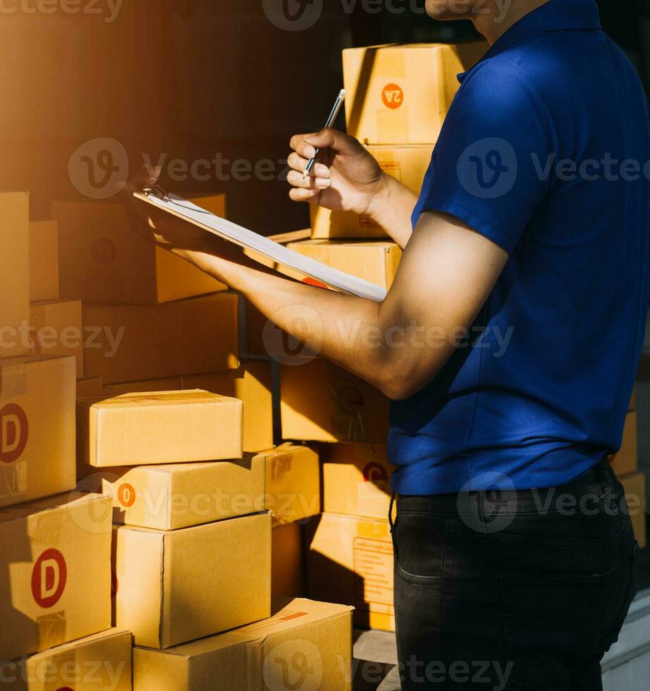 Delivery man with cardboard box checking document list In van and parcels on seat outside the warehouse. photo