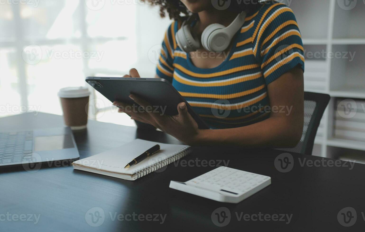 Young adult happy smiling Hispanic Asian student wearing headphones talking on online chat meeting using laptop in university campus or at virtual office. College female student learning remotely. photo