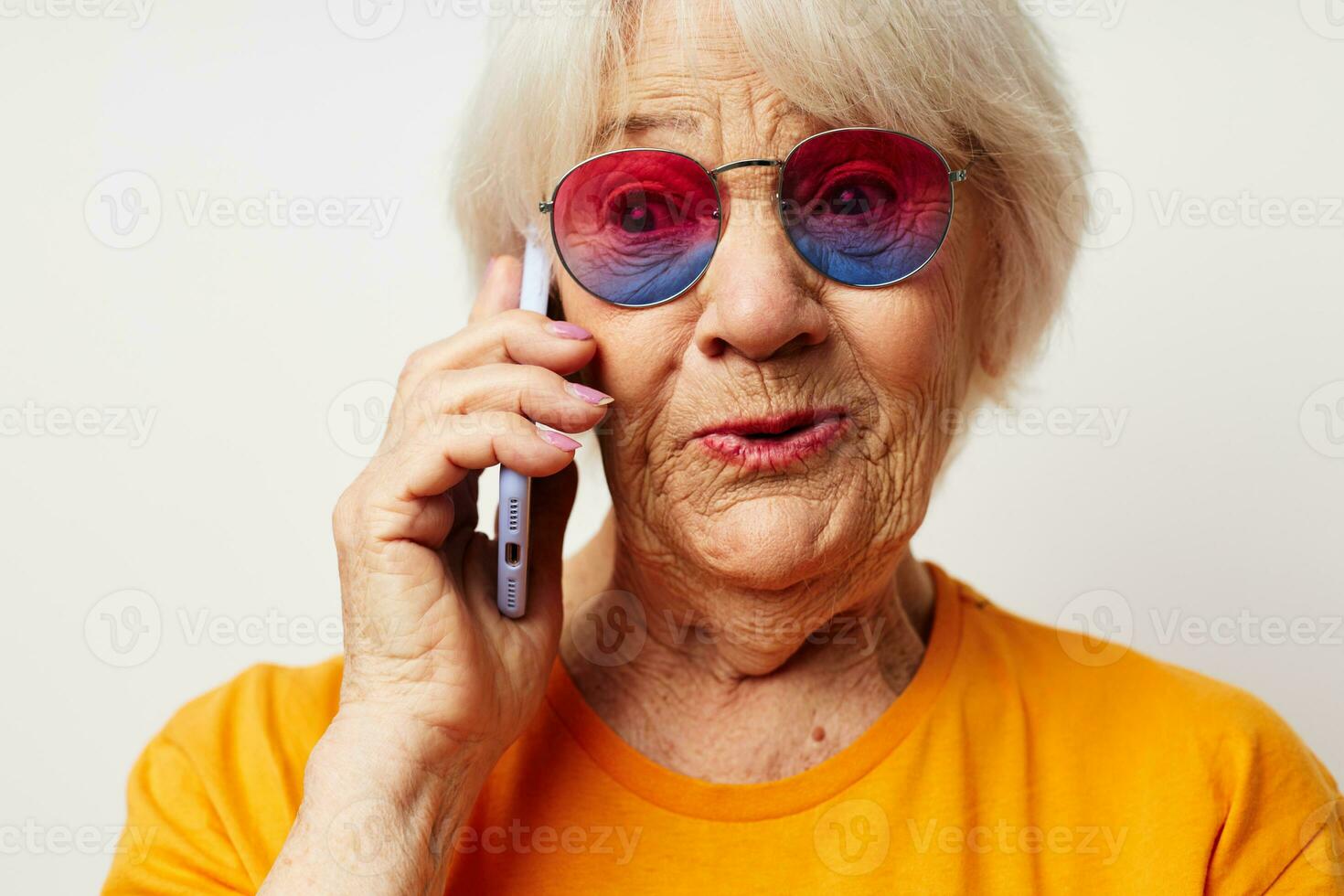smiling elderly woman in fashionable glasses with a smartphone in hand light background photo
