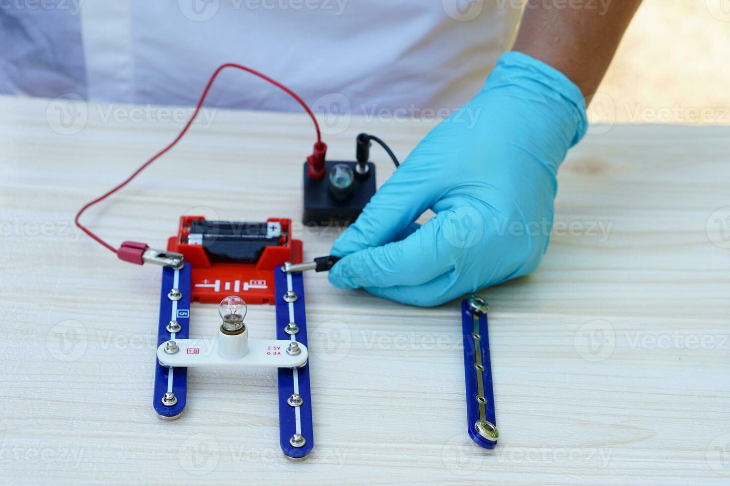Close up hands wear blue gloves holds mini light bulb kit to demonstrate science experiment about electricity circuit. Concept, scientific tools for education, lab lesson. Learning by doing. photo