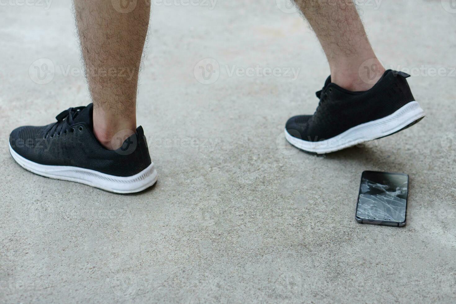 Closeup man wears black sport shoes, walking and his smartphone fell and broke on ground. Concept, damage with things in daily life from accident or careless. Mobile phone warranty claim for broken. photo