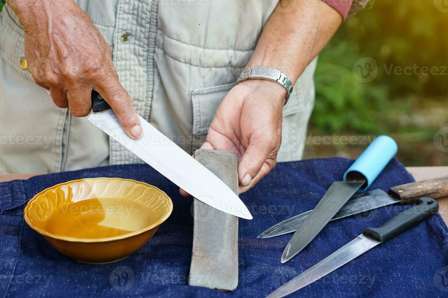 primer plano las manos del hombre afilan el cuchillo en el afilador de piedra de afilar o en la piedra de afilar. Concepto, herramientas de mantenimiento para cocinar, afilar cuchillos, no aburridos para un uso prolongado. estilo original foto