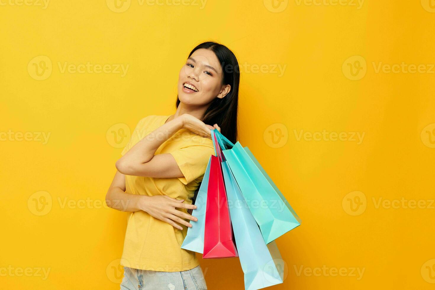 mujer con asiático apariencia en un amarillo camiseta con multicolor compras pantalones aislado antecedentes inalterado foto