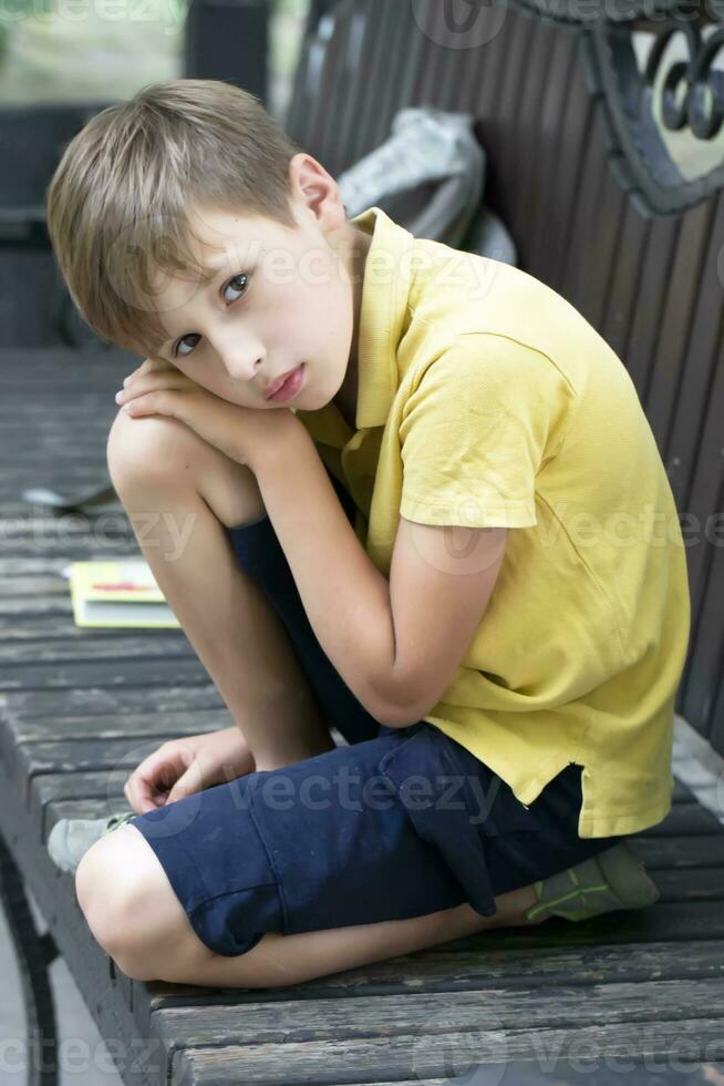 Sad little boy sits on a park bench. photo