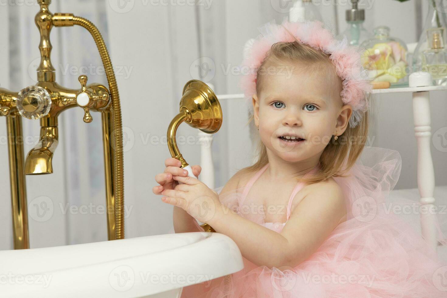 pequeño gracioso niña en un inteligente rosado vestir en el baño. foto