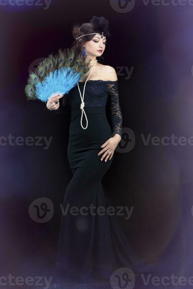 A beautiful girl dressed in the style of the 20-30s of the last century with a fan posing on a dark background. Vintage retro girl. photo