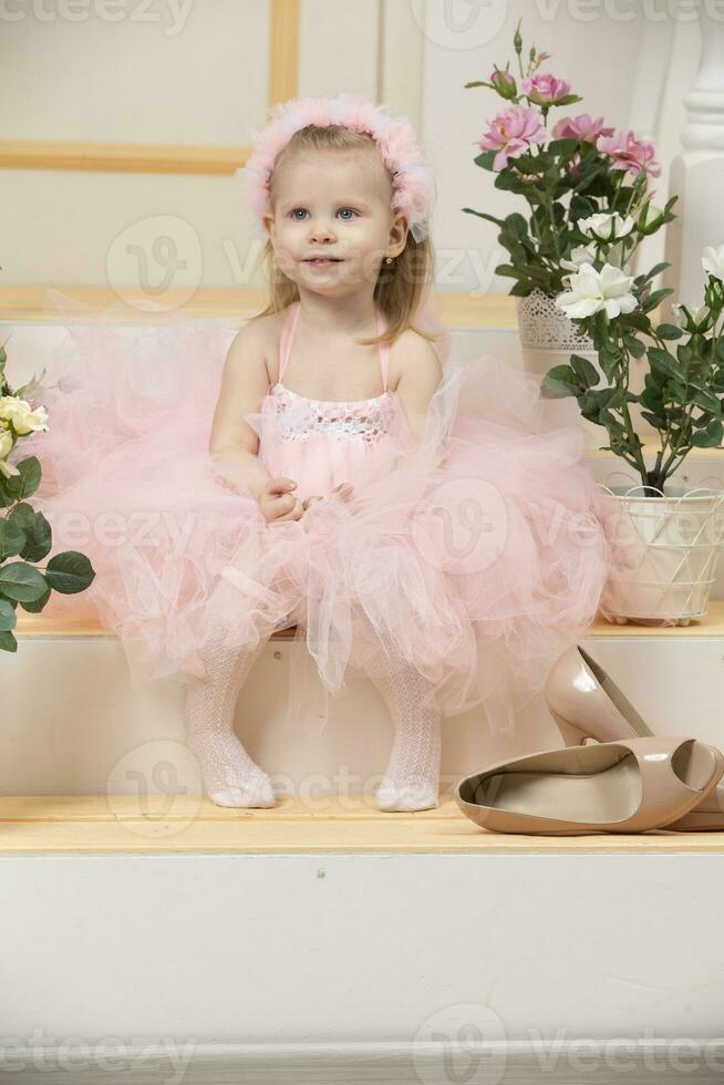 Two-year-old child. A beautiful little girl in a smart pink dress sits on the porch. photo