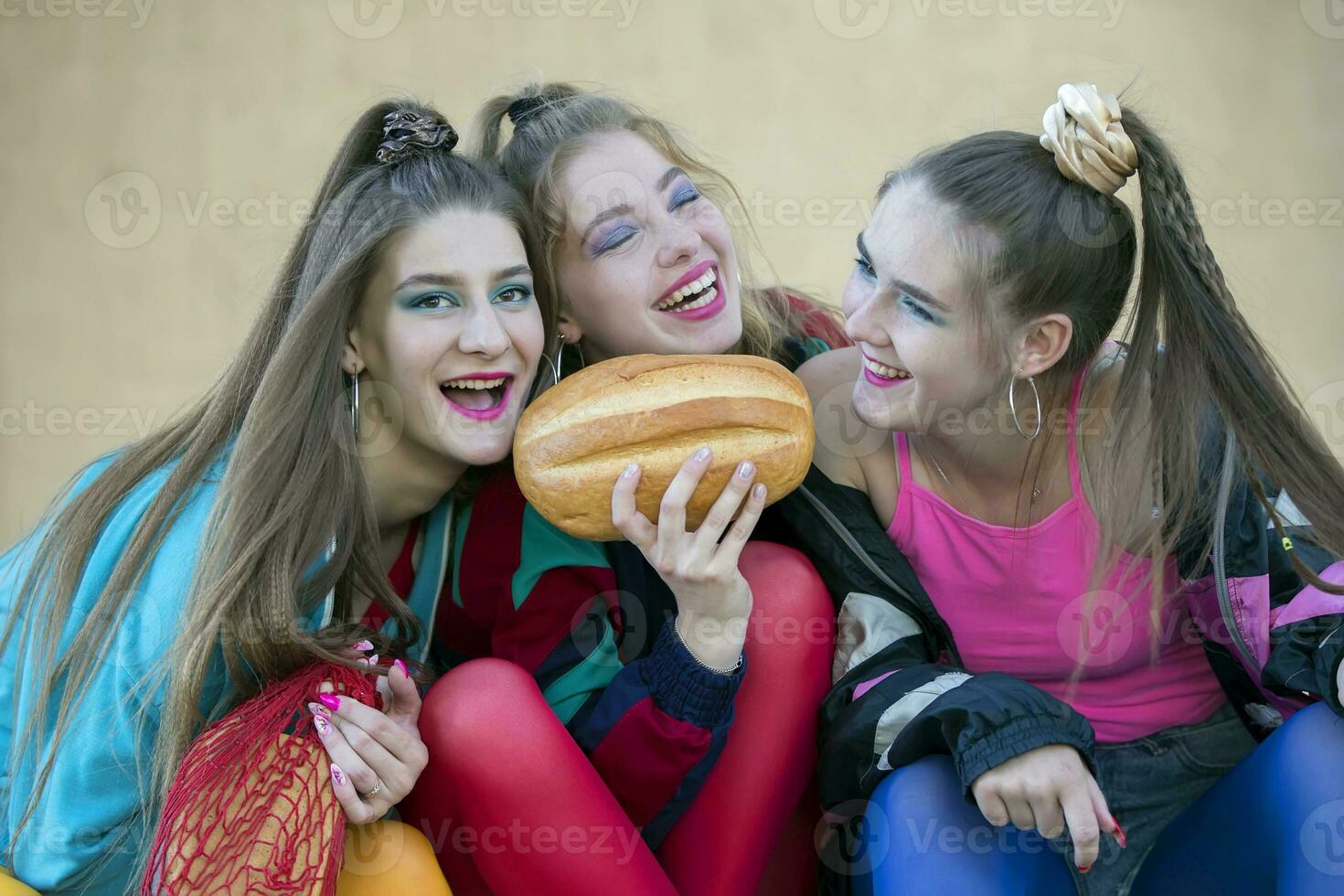 Tres bonito muchachas vestido en el estilo de el noventa son sentado en el pasos y compartiendo un rollo. foto