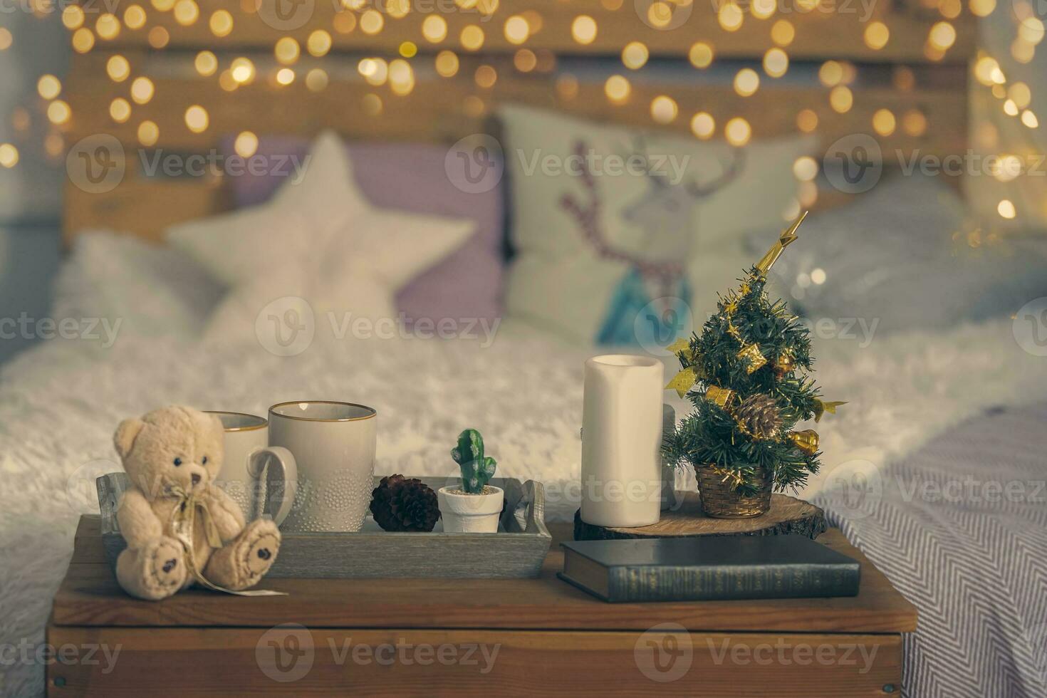 Christmas cozy interior background. A bed, a table with a cup and a toy, a little herringbone and bokeh lights. photo