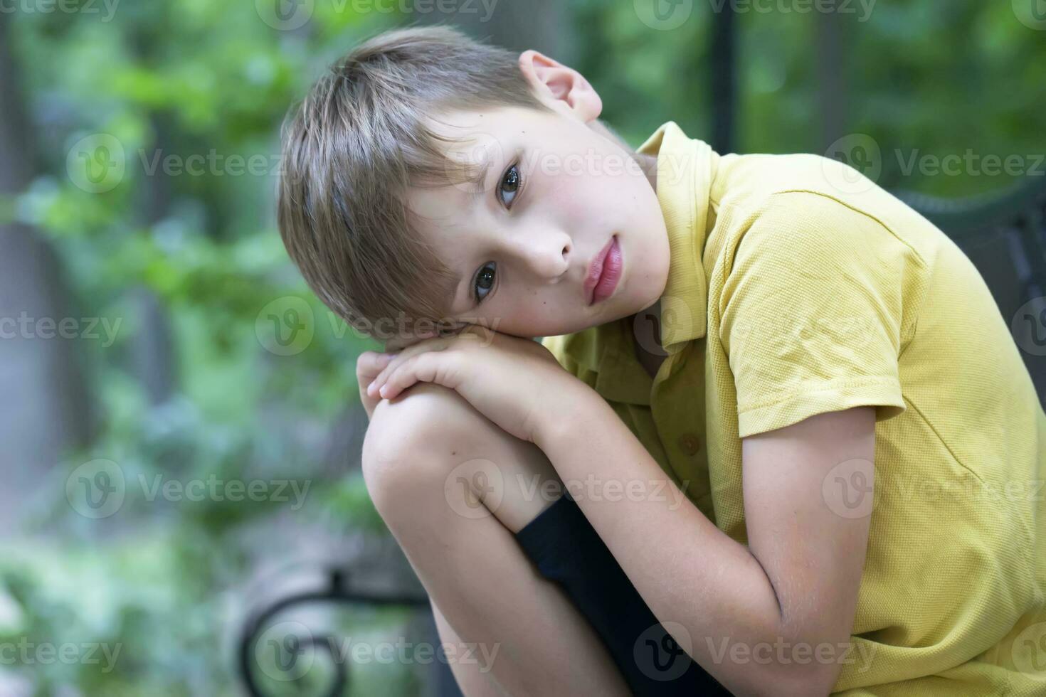 el triste pequeño chico poner su cabeza en su rodilla. el niño es aburrido. foto