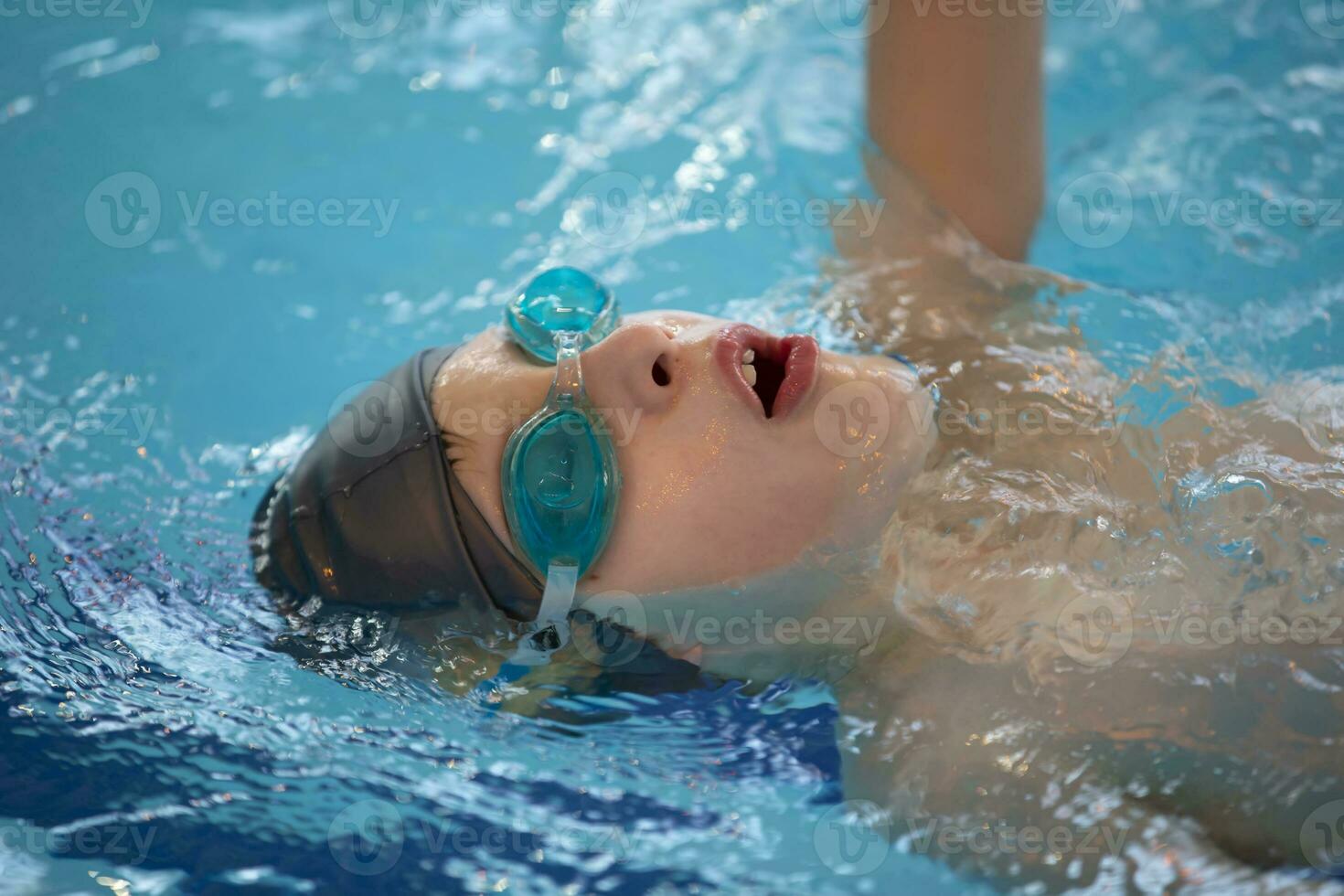 Boy in a swimming cap and swimming goggles in the pool. The child is engaged in the swimming section. photo