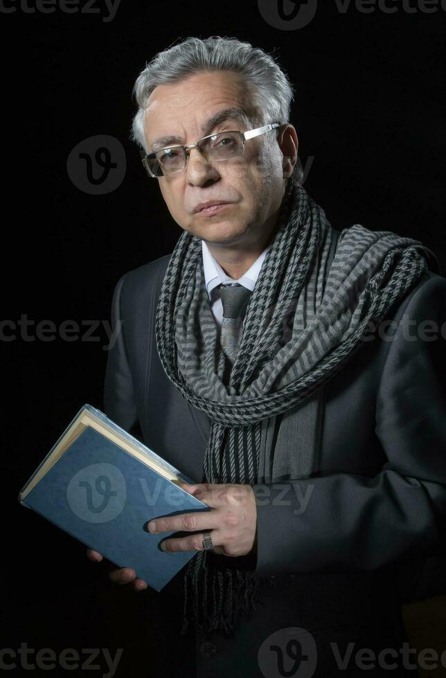 Portrait of an elegant elderly man with glasses and a book on a black background. photo