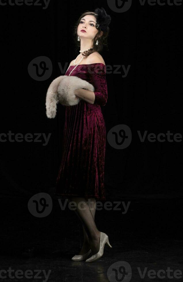 A beautiful girl dressed in the style of the 20-30s of the last century posing on a dark background. photo