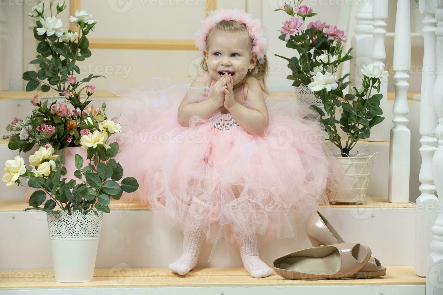 Two-year-old child. A beautiful little girl in an elegant pink dress and high heel shoes sits on the porch. photo