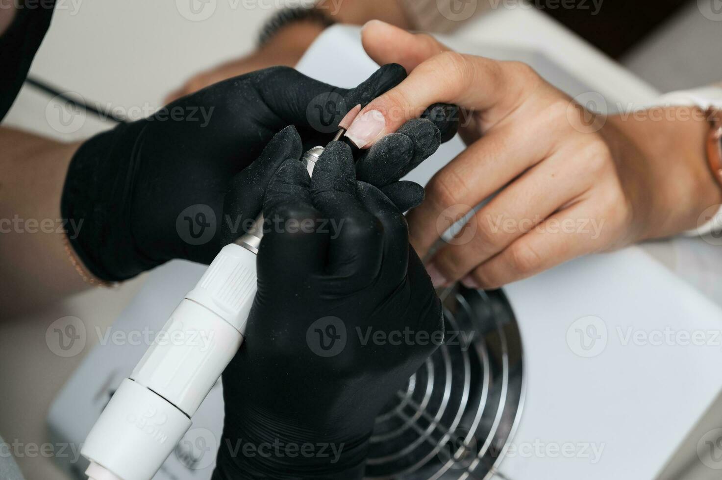 A close-up of a manicure master processing the nail surface with a cutter on an electric machine, removing burrs. The concept of a professional manicure salon photo