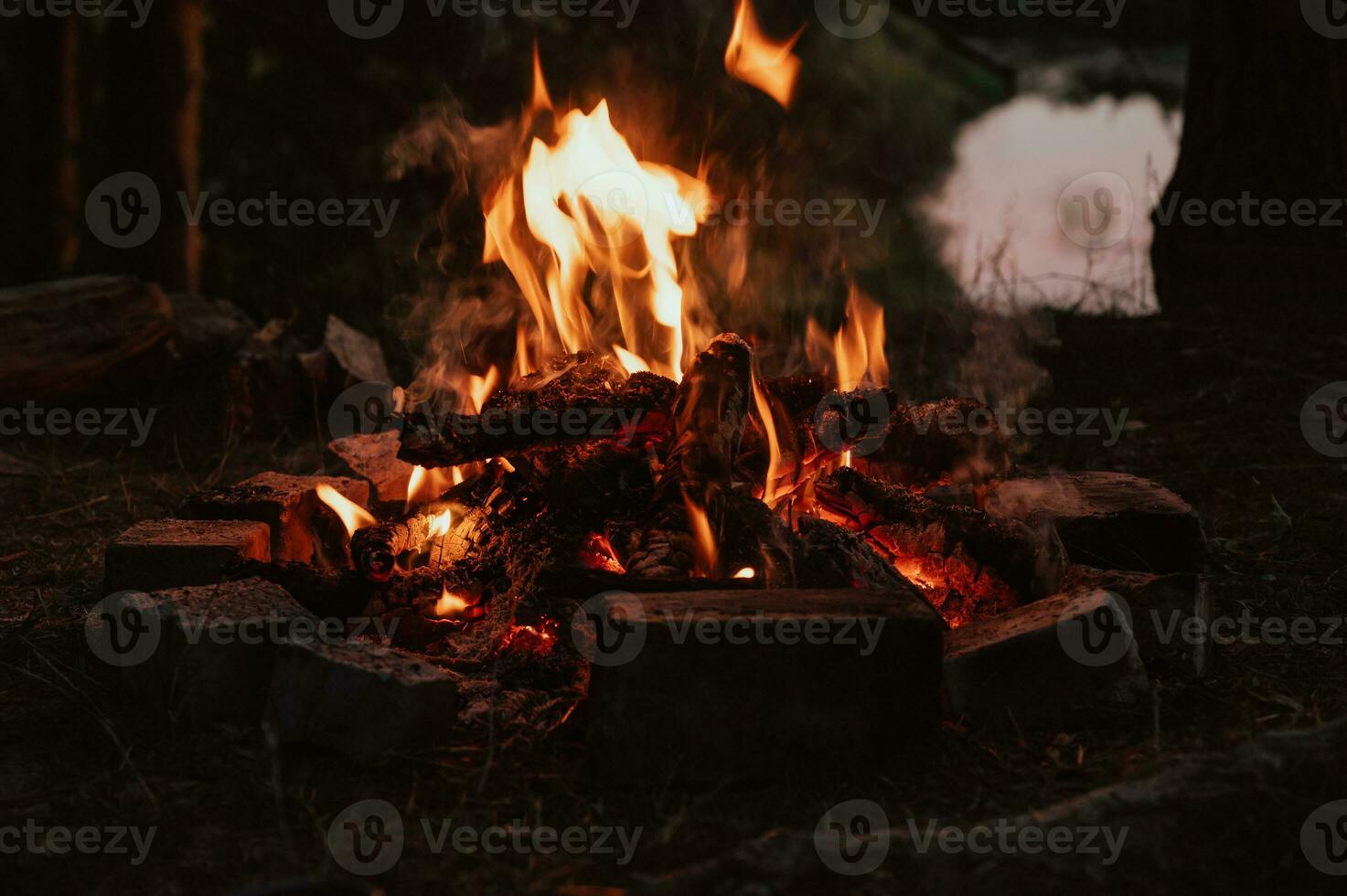 A bonfire in close-up, flames, charred pieces of logs and ashes in the open air against the landscape. Camping. photo