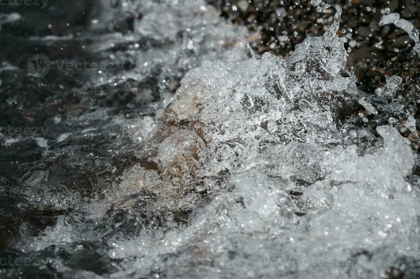 Small stones in azure sea water close-up. A picture of the sea surf. Ocean surf among the rocks. Background of the tide. Sea foam photo