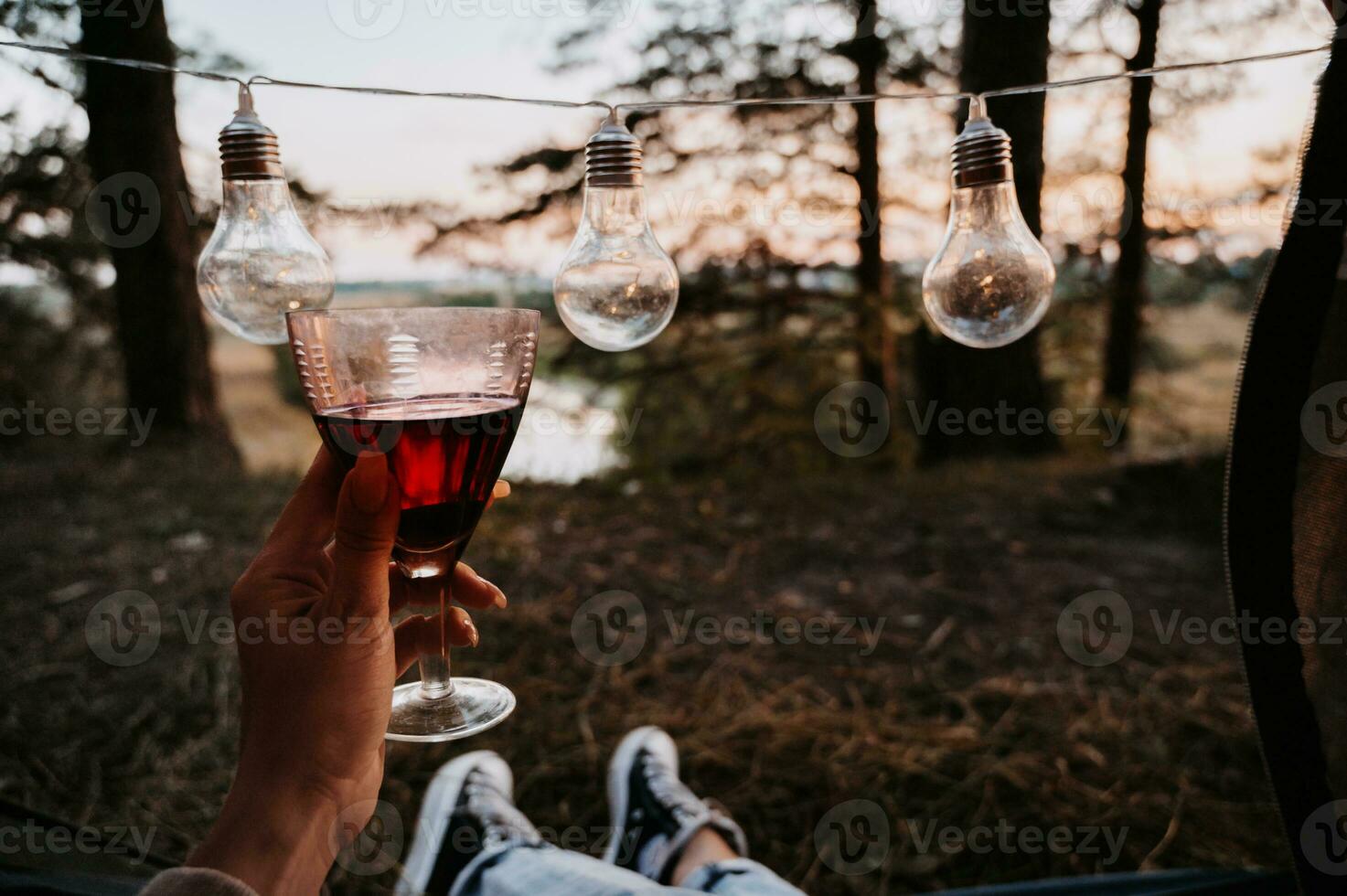 A close-up photo of the intentions of women's legs. The girl has a glass of wine or water in her hands. The concept of a tourist trekking expedition. View from the tent to the landscape