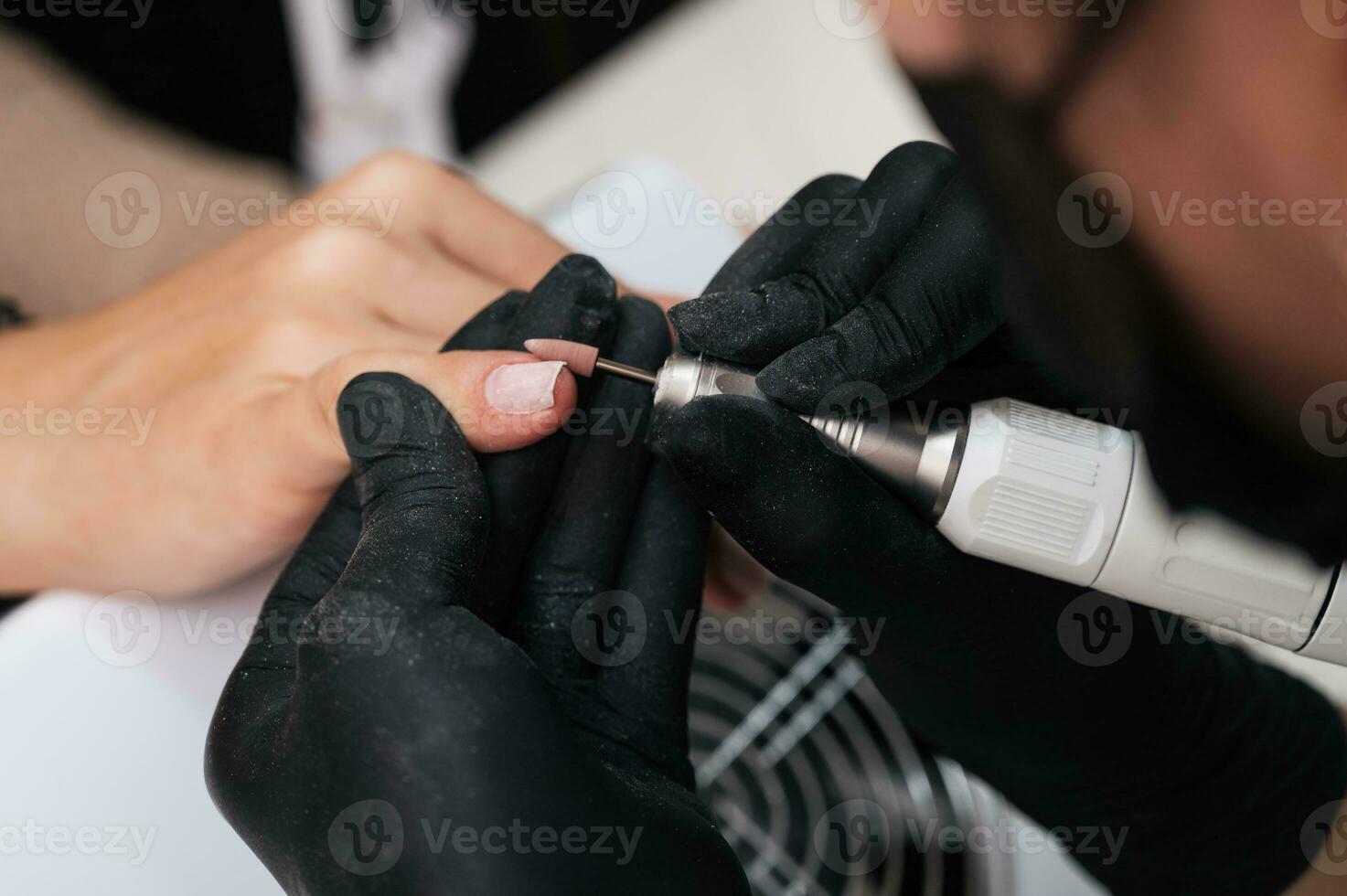 A close-up of a manicure master processing the nail surface with a cutter on an electric machine, removing burrs. The concept of a professional manicure salon photo