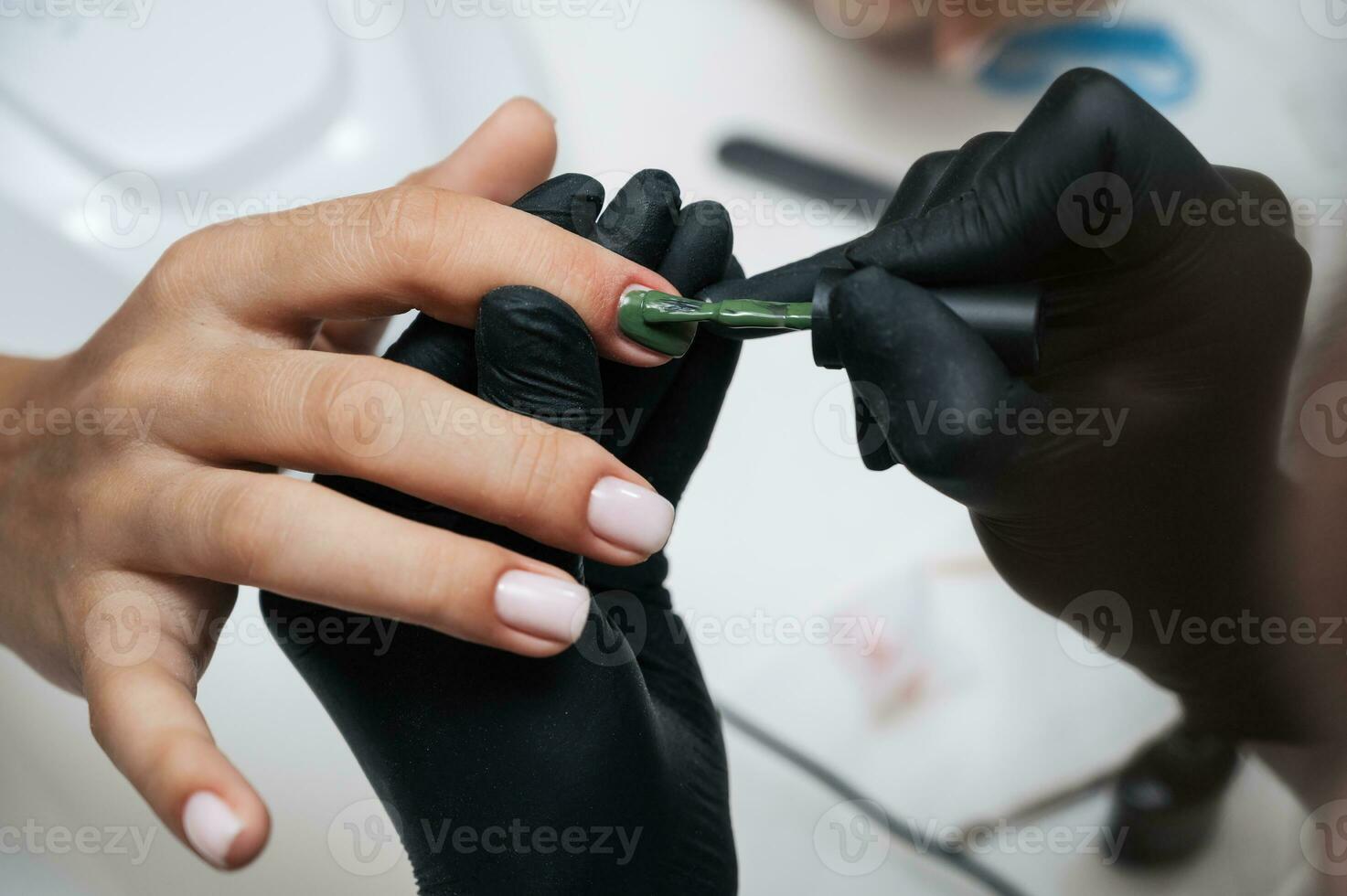 Manicure service. Close-up. Applying green varnish . The manicurist paints her nails with a transparent gel polish. Well-groomed nails. Professional salon hand care. photo