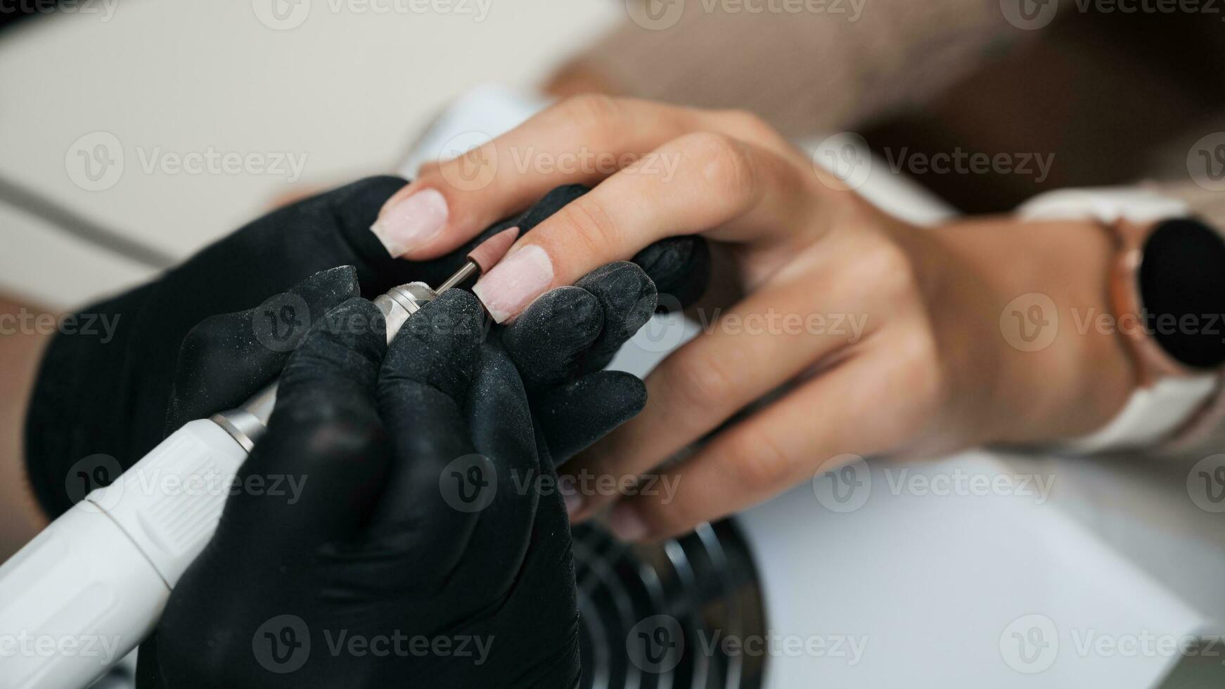 A close-up of a manicure master processing the nail surface with a cutter on an electric machine, removing burrs. The concept of a professional manicure salon photo