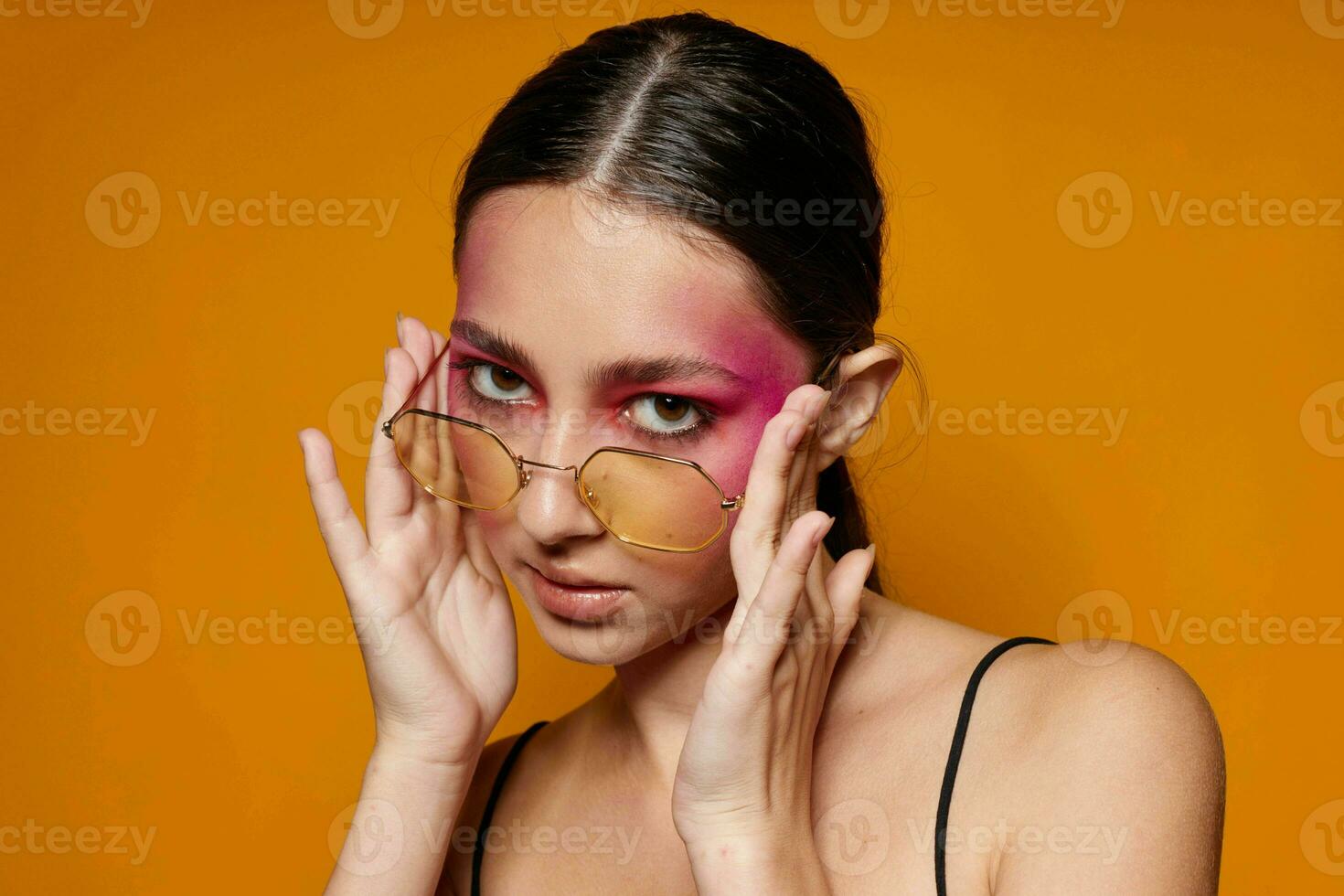 Portrait of beautiful young woman fashion glasses pink face makeup posing attractive look yellow background unaltered photo