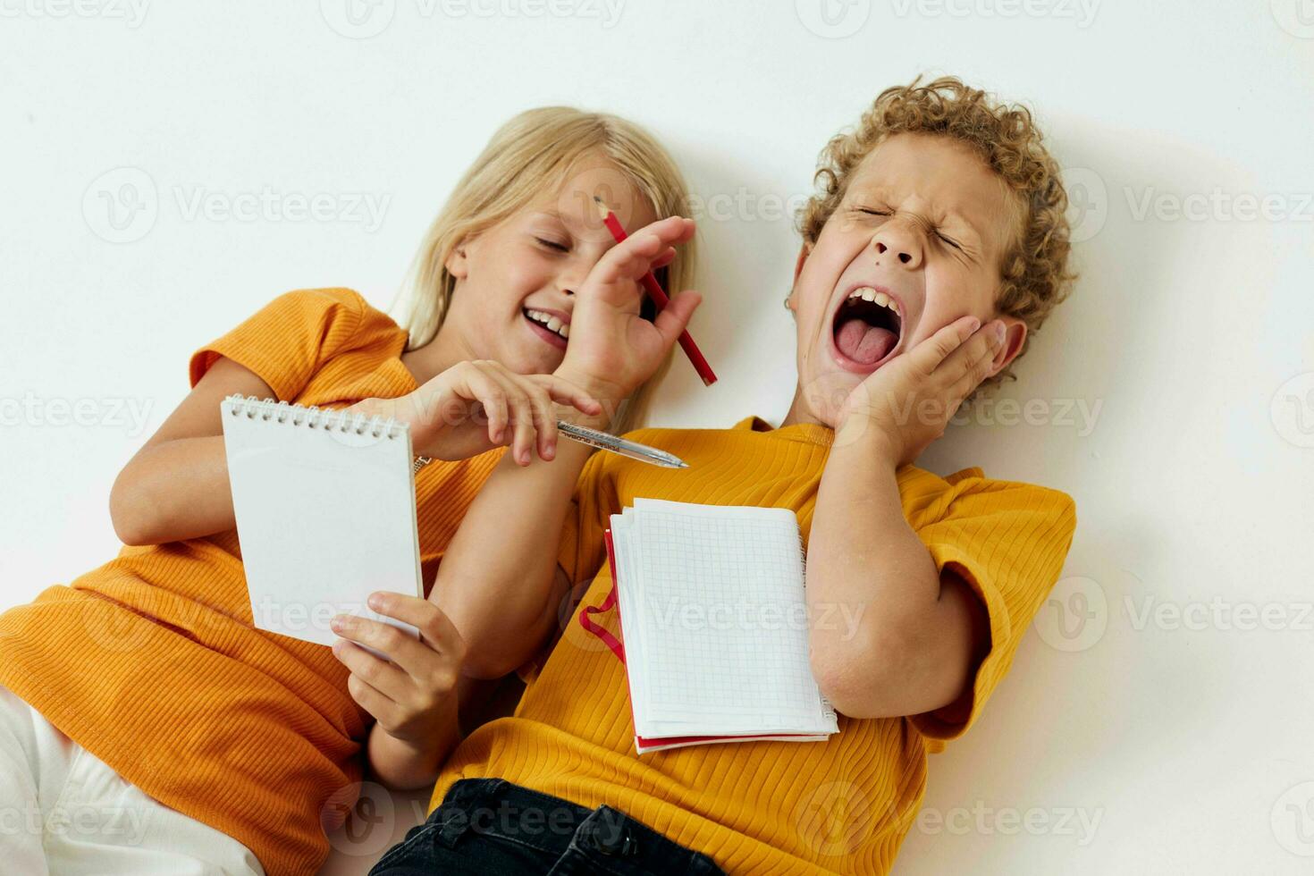 pequeño niños mentira en el piso con libretas y lapices aislado antecedentes inalterado foto