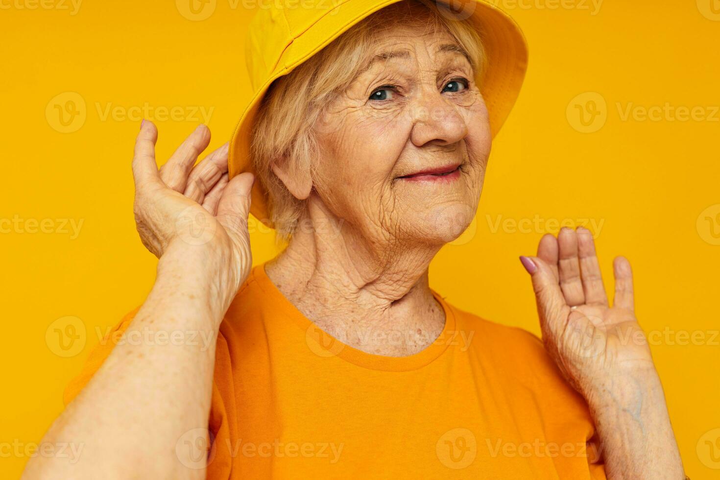Portrait of an old friendly woman in yellow t-shirts hat posing cropped view photo