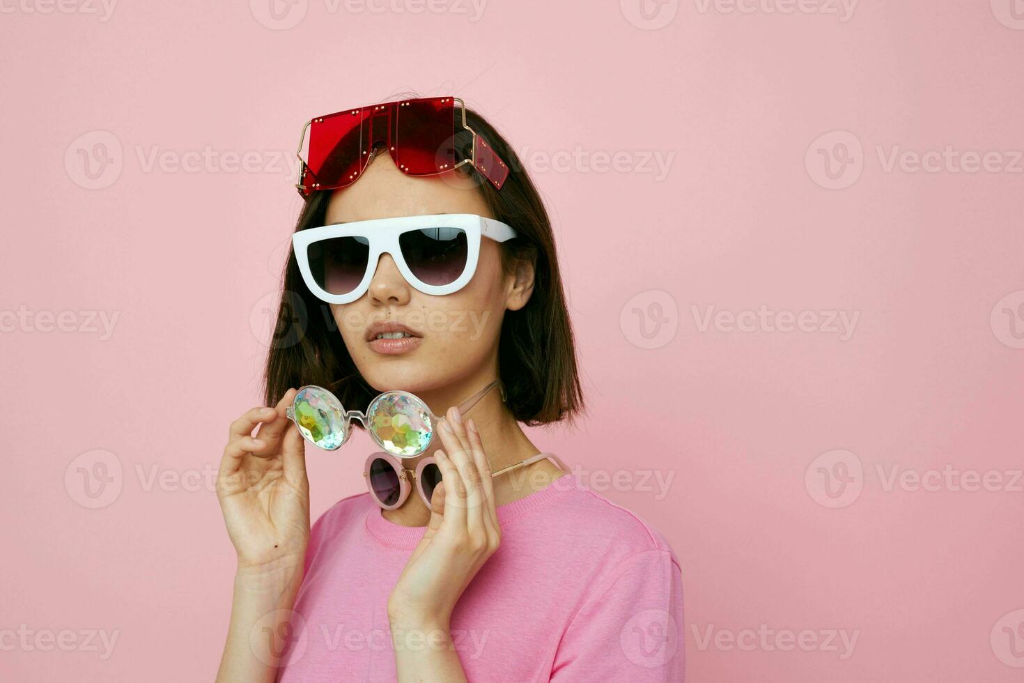 short haired brunette a lot of glasses on the face in a pink t-shirt pink background photo