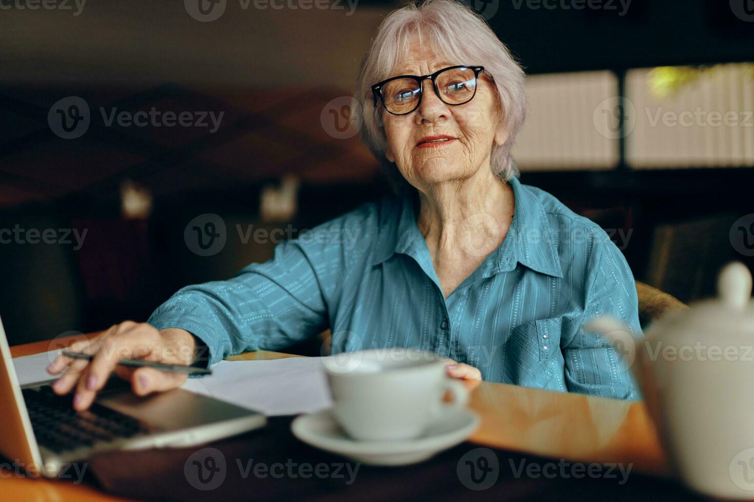 Beautiful mature senior woman with glasses sits at a table in front of a laptop unaltered photo