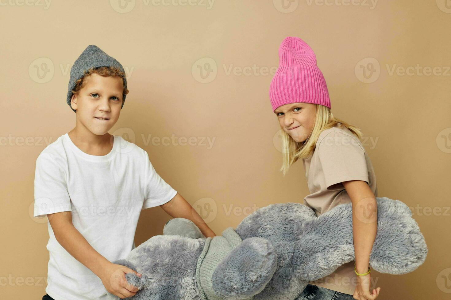 Photo of two children in multi-colored hats entertainment posing beige background