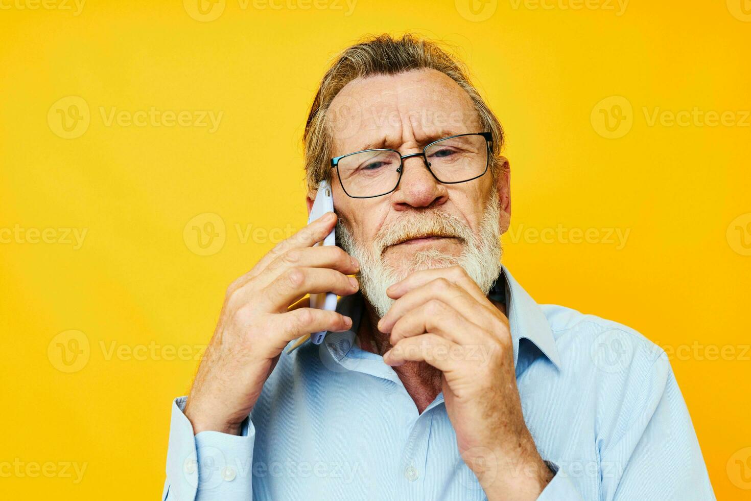Photo of retired old man talking on the phone posing close-up yellow background