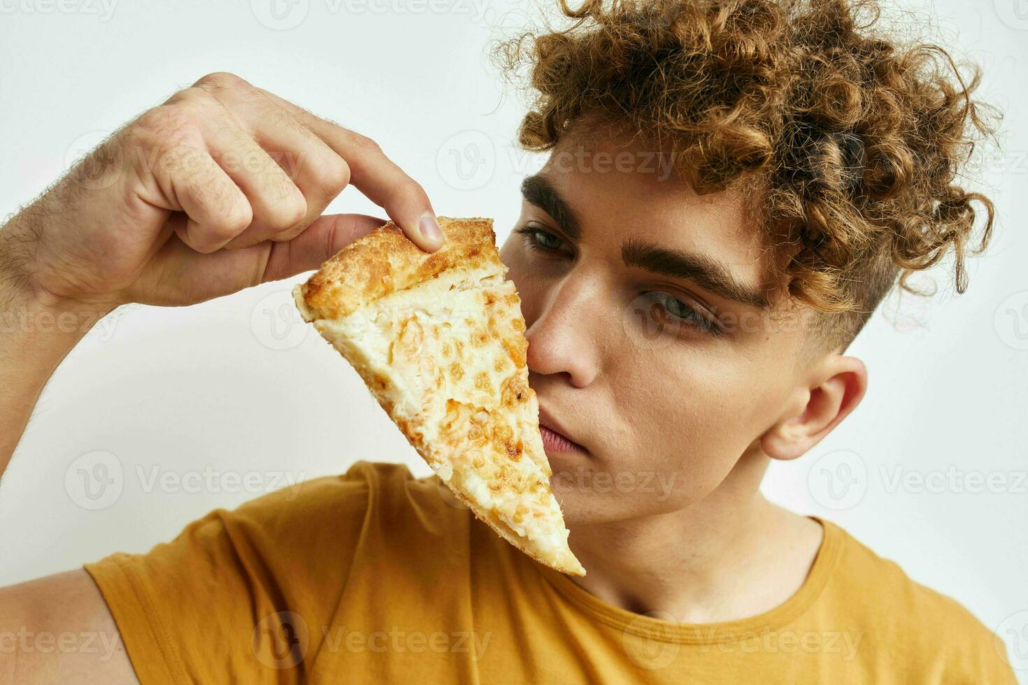 rizado chico en un amarillo camiseta comiendo Pizza estilo de vida inalterado foto