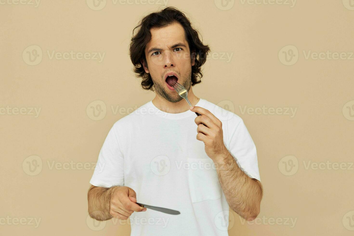 handsome man in a white T-shirt with knife with fork beige background photo