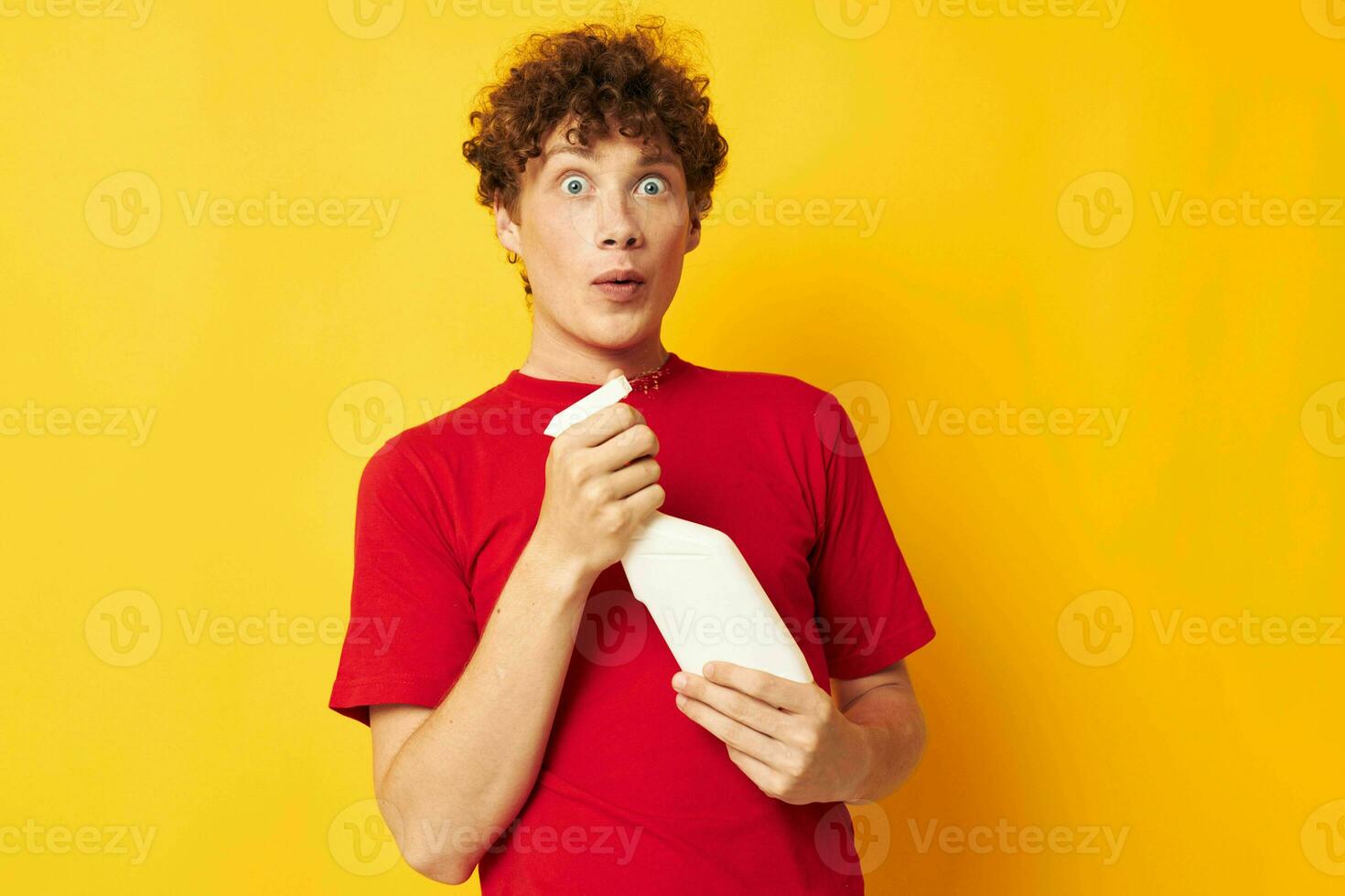 Young curly-haired man in a red t-shirt detergents in hands posing Lifestyle unaltered photo