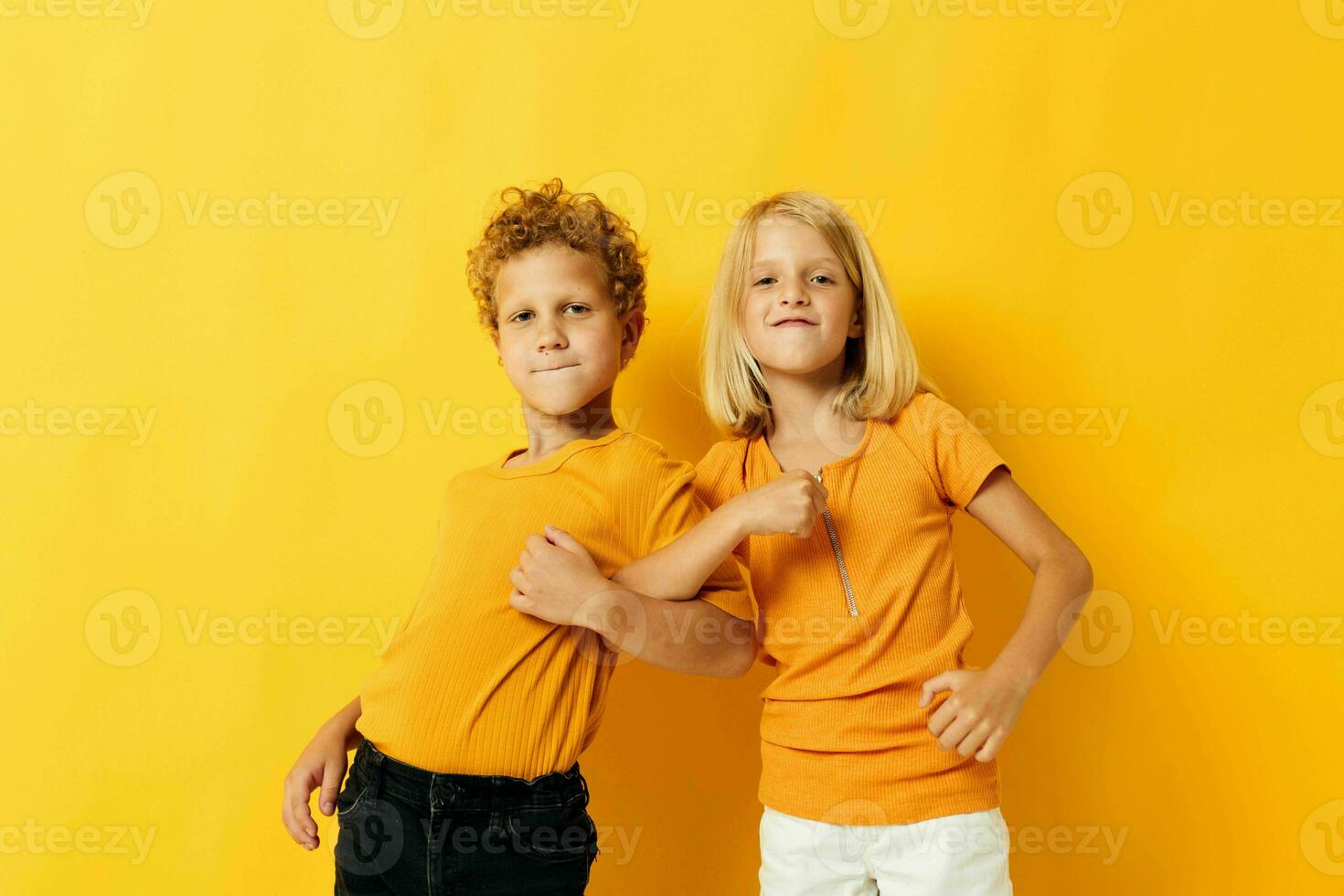 Boy and girl in yellow t-shirts standing side by side childhood emotions yellow background photo