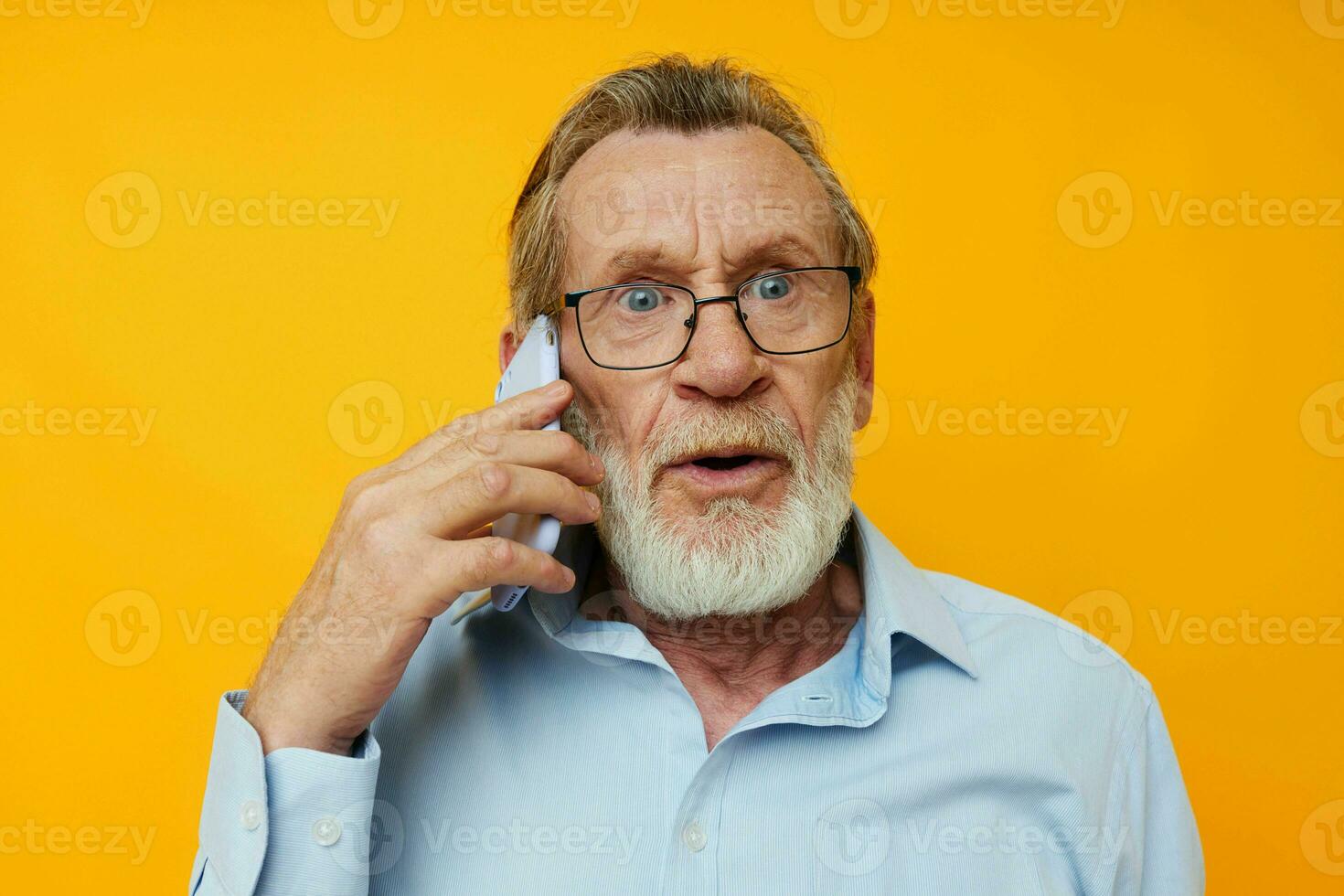 Photo of retired old man talking on the phone posing close-up yellow background