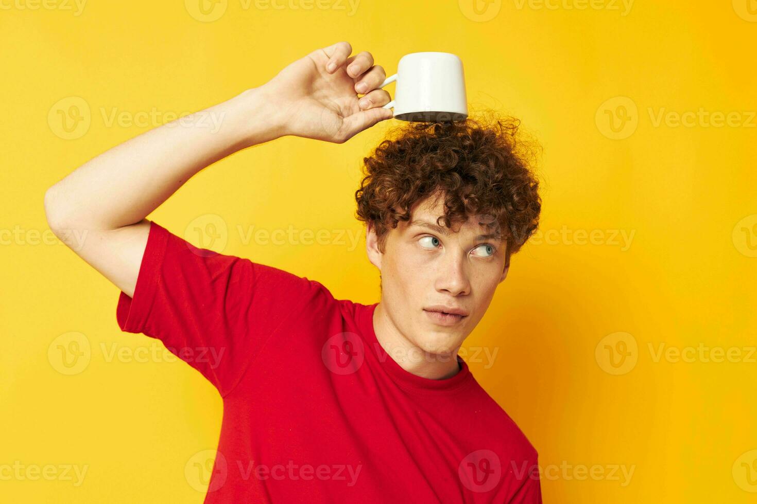 portrait of a young curly man posing with a white mug and in the hands of a drink yellow background unaltered photo